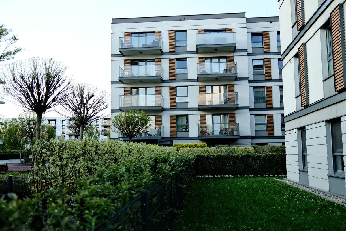 Modern apartment building with stacked balconies behind a clipped hedge