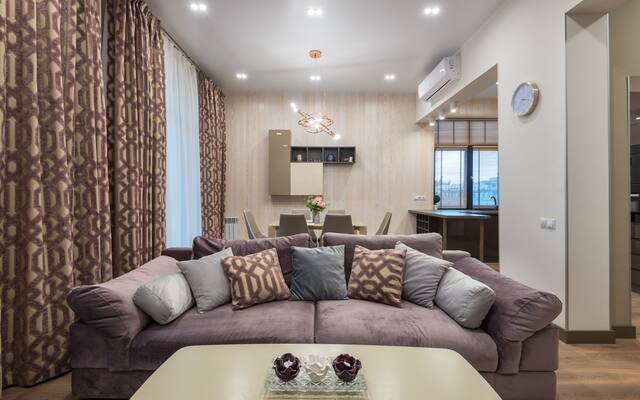 Furnished suite living room with a long sofa, floor-length curtains and a dining table