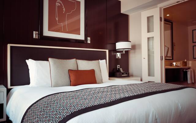 Hotel room with a made bed, headboard lighting and an open bathroom doorway