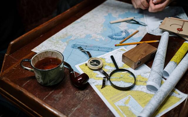 Folded maps, a compass, a magnifier and a coffee cup on a wooden desk