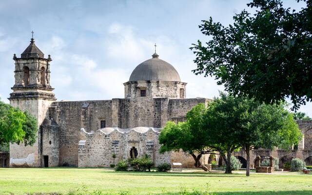 The dome and bell tower of Mission San Jose above its lawn on the San Antonio south side