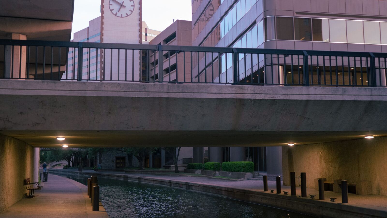 Office towers and a clock tower above a quiet canal walk in downtown San Antonio
