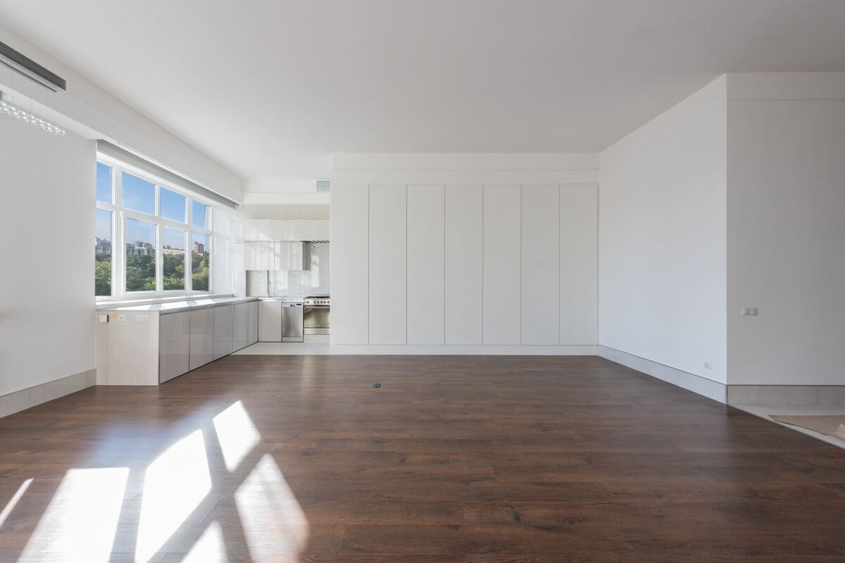 Empty apartment room with sunlight across a dark wood floor