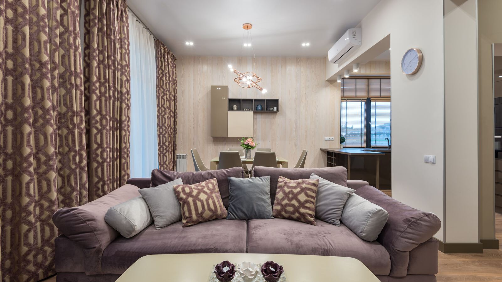 Furnished suite living room with a long sofa, floor-length curtains and a dining table