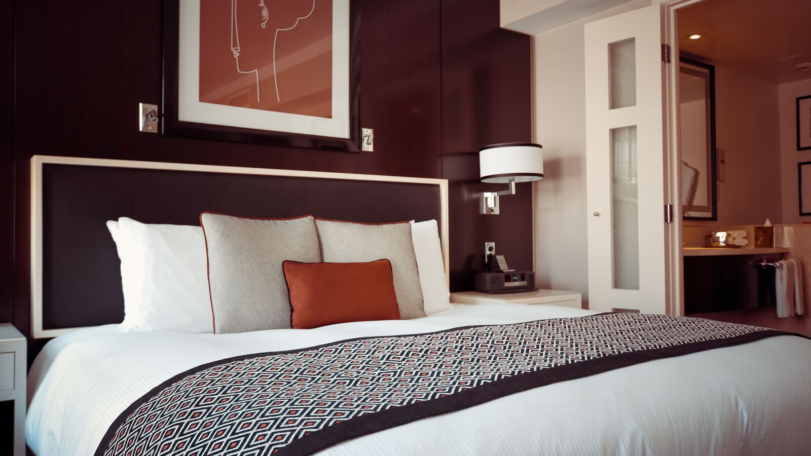 Hotel room with a made bed, headboard lighting and an open bathroom doorway