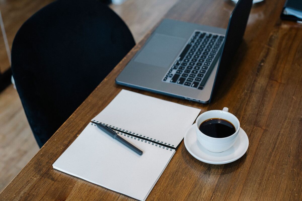 Laptop, ruled notebook and a coffee cup on a wooden table
