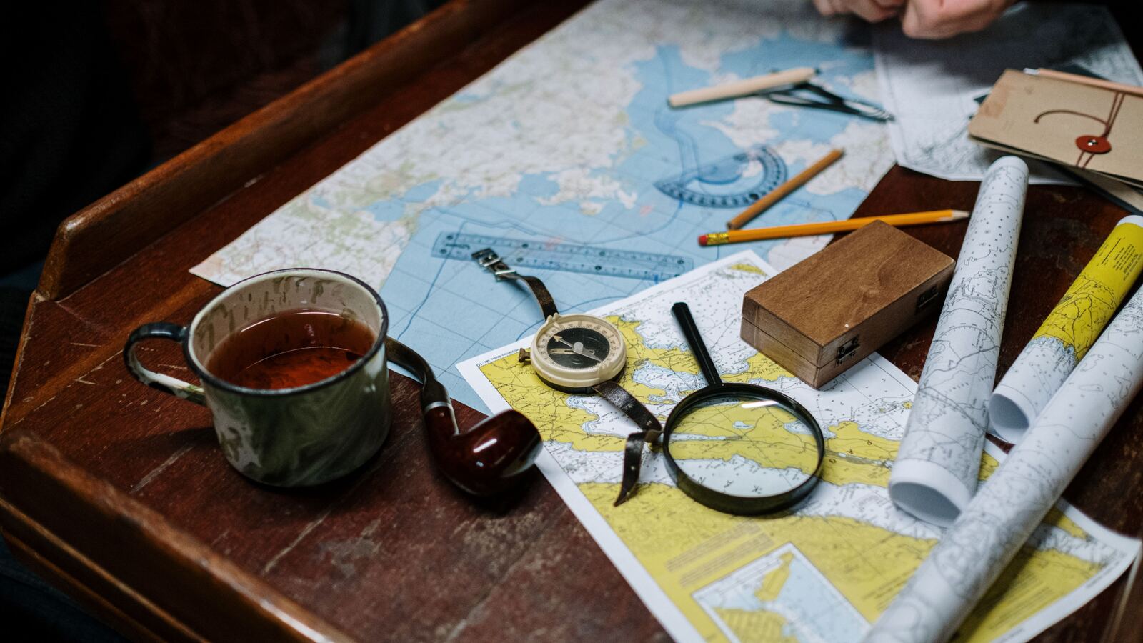 Folded maps, a compass, a magnifier and a coffee cup on a wooden desk